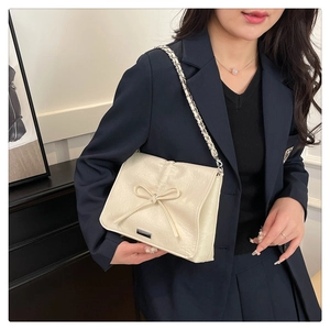 Detail of cream white shoulder bag with ribbon bow and silver chain strap on model