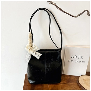 Detail of black textured leather shoulder bag with delicate white lace bow accessory