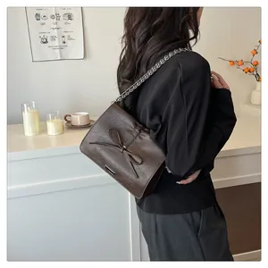 Detail of dark brown leather crossbody bag with bow decoration and silver metal accents