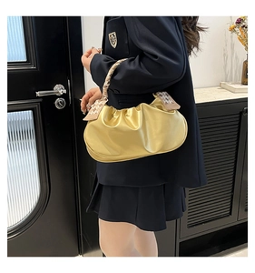 Dettaglio borsa gialla a pieghe con foulard a quadri sul manico indossata al braccio