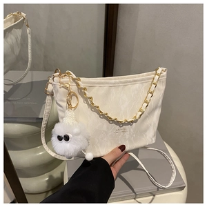 Close-up of cream textured crossbody bag with gold chain and plush ball pendant