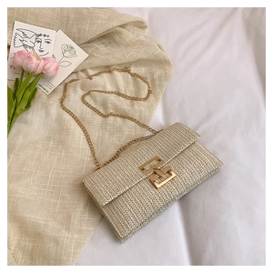 Detailed view of woven straw envelope bag with gold chain strap on white linen