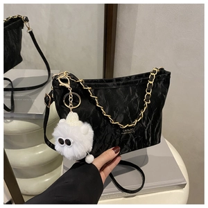 Close-up of black pleated texture shoulder bag with gold chain and plush toy charm