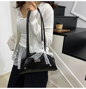 Detail of glossy black patent leather shoulder bag with white lace bow and metal plaque