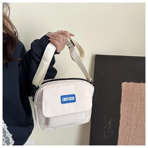 Close-up of white canvas crossbody bag with blue FANYISSA brand label and wide shoulder strap