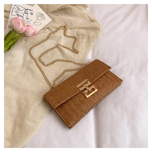 Detail of woven straw shoulder bag with golden H-buckle and chain strap in a warm setting