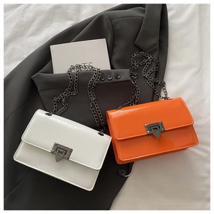 Detail von glänzenden Lackleder-Umhängetaschen in Weiß und Orange mit Metallverschluss