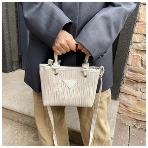 Close-up of woven straw handbag with white leather trim and fashion logo detail