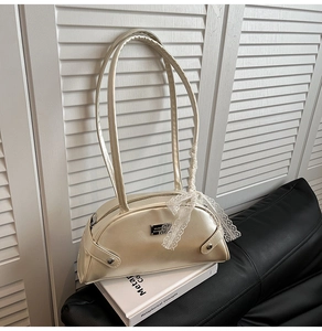 Detail of champagne gold shoulder bag with white lace bow and metal plaque on a book