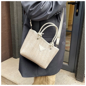 Detail of color-block woven straw bucket bag with leather handles and metallic logo badge