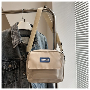 Detailed macro view of the front pocket and logo on this beige canvas crossbody bag
