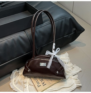 Macro shot of dark brown polished leather bag with white lace bow and metal logo plate