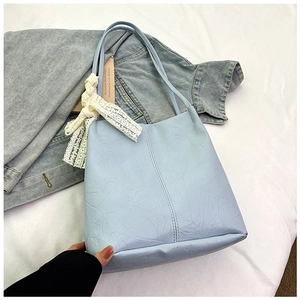 Detail of light blue textured leather tote bag featuring a delicate white lace bow accent