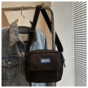 Detail of minimalist black nylon crossbody bag with blue brand logo patch and pocket