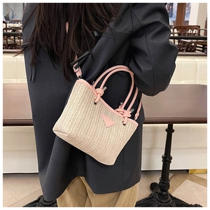 Detail of hand-woven straw bucket bag with pink leather trim worn over a grey blazer