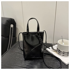 Mini sac à main noir brillant avec poignées tressées et bandoulière dans un décor moderne