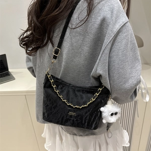 Black ruched shoulder bag with gold chain and plush charm shown in a minimalist room
