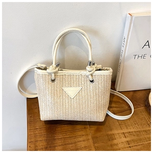 Detailed view of woven straw bucket bag with white leather straps and fashion label