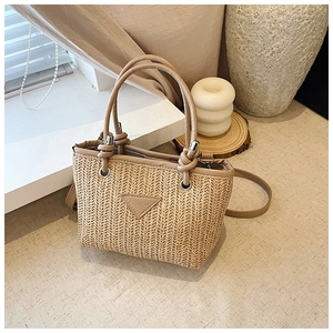 Detail of woven straw tote bag featuring a leather triangle logo and sturdy top handles