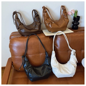 Detail view of four pleated crescent bags with knotted strap on a leather sofa