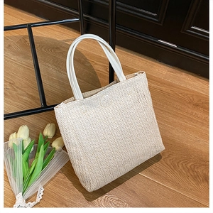 Primo piano della borsa tote in paglia intrecciata beige con manici bianchi e fiori