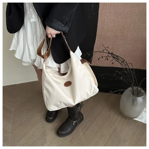 Close-up of cream nylon hobo bag with round fashion logo patch and wide strap