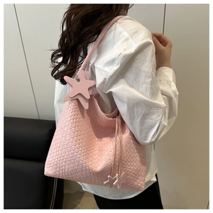 Détail d'un grand sac fourre-tout rose tressé avec breloques étoiles sur la bandoulière