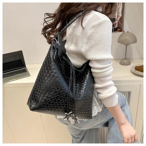 Détail d'un sac à bandoulière tressé noir avec breloque étoile et fermeture à cordon