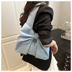 Détail du sac cabas en denim bleu clair avec grand nœud porté à l'épaule par un mannequin