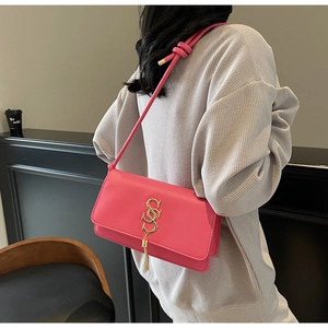 Detail of pink leather crossbody bag with golden S-shaped buckle and tassel on a model