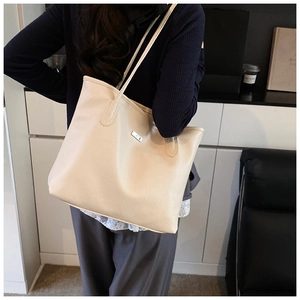 Détail de la texture en cuir grainé beige et logo métallique sur un grand sac cabas