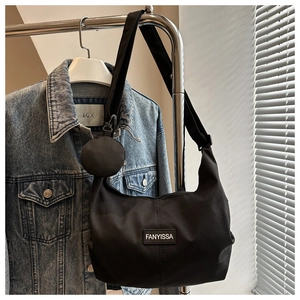 Détail d'un sac bandoulière en nylon noir avec pochette ronde sur un cintre en métal