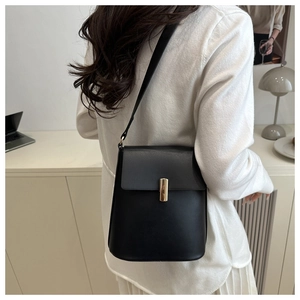 Détail du sac seau noir en cuir avec fermoir doré vertical porté par un mannequin