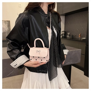 Détail du mini sac rose à pois avec nœud papillon argenté porté sur une veste en cuir