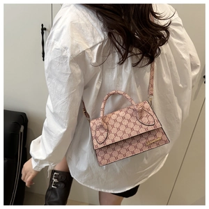 Détail d'un sac à bandoulière rose avec motif monogramme porté par un mannequin en ville
