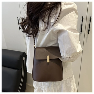 Sac à bandoulière minimaliste en cuir marron foncé avec fermoir doré porté par un modèle