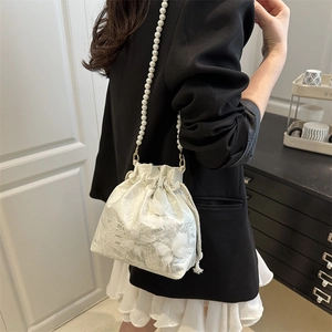 Chic white lace bucket bag with pearl strap and floral embroidery shown on shoulder