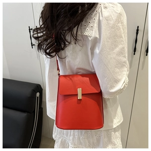 Détail du sac bandoulière rouge avec fermoir doré porté sur un haut en dentelle blanche