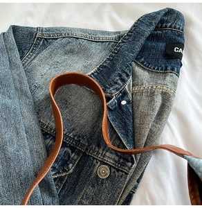 Detail of washed denim tote with silver CA brand label and metallic button buckle