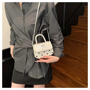 Détail d'un mini sac à bandoulière blanc à pois avec un fermoir papillon en métal argenté