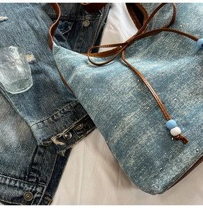 Detail of light blue denim bucket bag with scattered rhinestones and brown bow strap