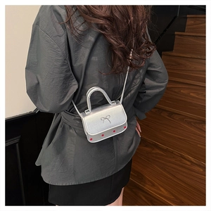 Détail du mini sac argenté avec nœud embossé et pois rouges porté par le mannequin