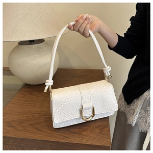 Detailed view of white crocodile pattern bag with golden hardware and braided strap
