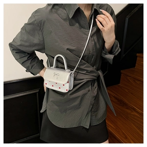 Sac bandoulière argenté à pois avec détail papillon porté par un mannequin en intérieur