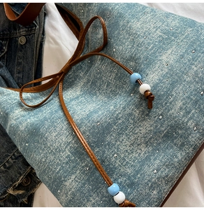 Detail of blue denim tote bag with silver rhinestones and brown leather beaded strap