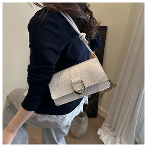 Close-up of white woven shoulder bag featuring a gold U-shaped metal buckle and knot strap