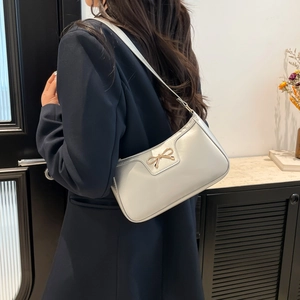 Silver glossy baguette bag with golden bow accessory worn as an underarm shoulder bag