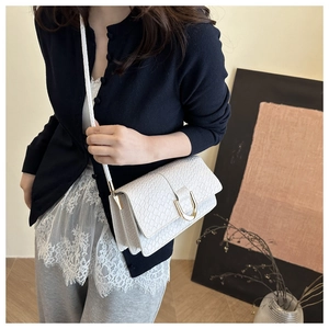 Close-up of white woven leather texture and gold horseshoe buckle on the shoulder bag