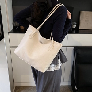 Sac fourre-tout beige minimaliste en cuir à motif litchi porté par un mannequin