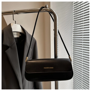 Detail der minimalistischen schwarzen Leder-Baguette-Tasche mit goldener Beschriftung